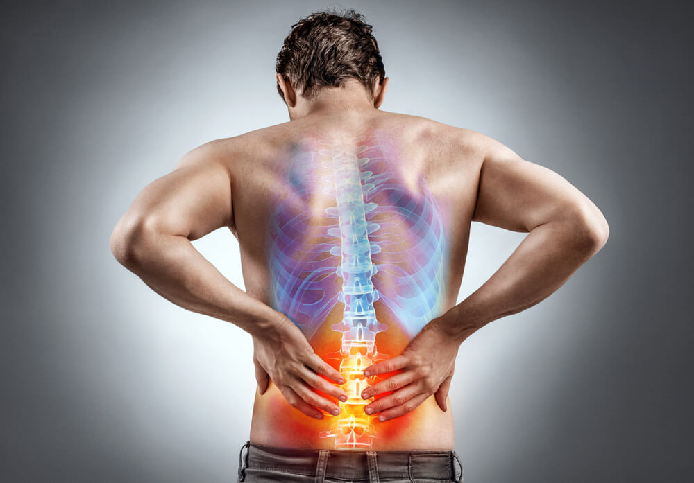 A woman's back being gently handled by a doctor as she sits. An illustration of a spine is overlaid over her back.